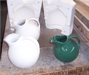 This photo shows a ball jug in 3 stages.  The large white jug is from the pre-formed mold where the clay slip is poured into mold. The smaller white jug in the back ready to be fired. The green jug is shown as final product after color s sprayed on jug and then fired.